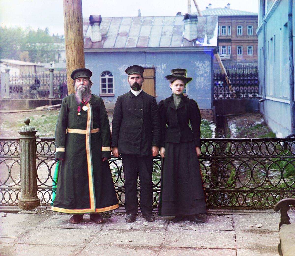 Цветная фотография начала века: пожилой мужчина, сын и внучка стоят у ограды набережной