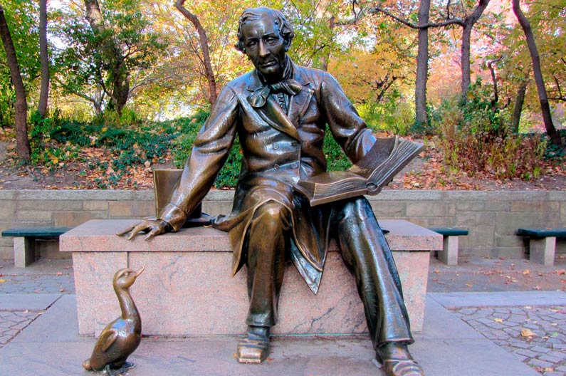 Бронзовый памятник: Андерсен сидит с раскрытой книгой, у его ног стоит утёнок, вокруг осенний парк