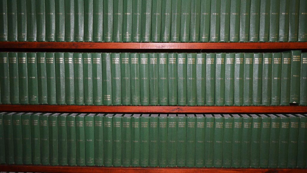 Три полки библиотеки, плотно уставленные одинаковыми книгами в зелёных переплётах