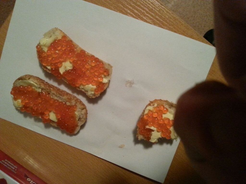 Три бутерброда с маслом и красной икрой на белом листе бумаги, рядом рука