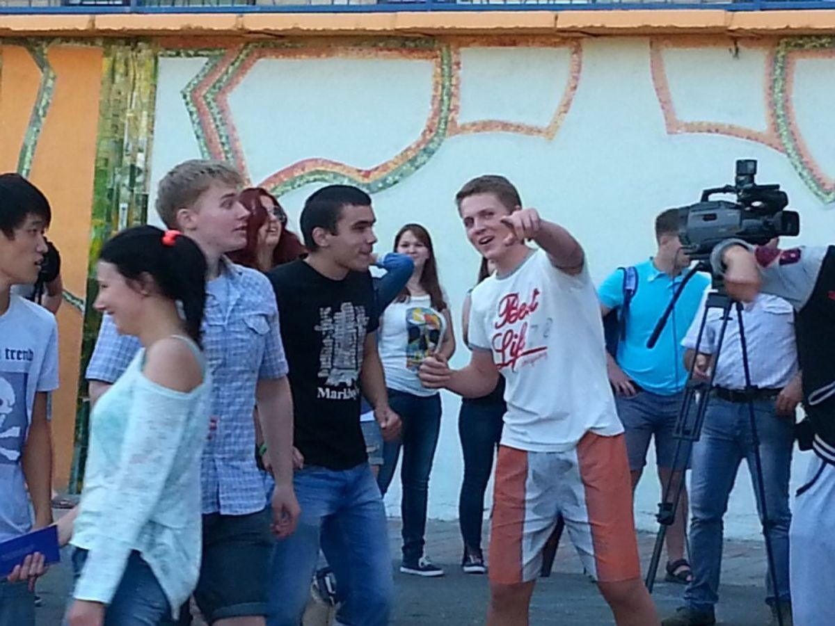 Компания подростков на улице, один из парней смеётся и показывает пальцем в камеру